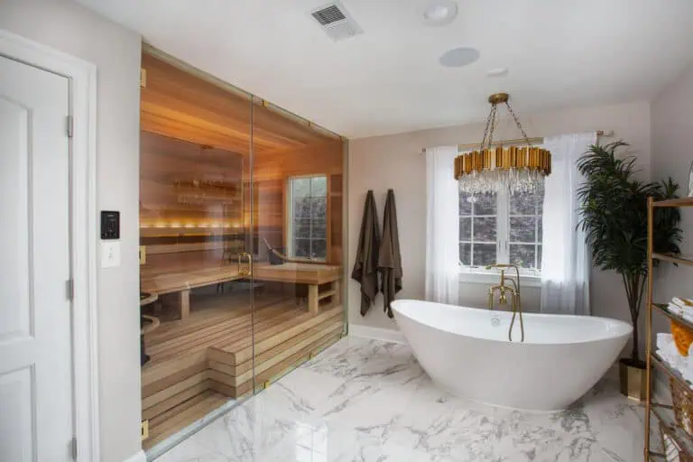 Built-in sauna with a full glass front, wood benches, and backrest lighting beside a freestanding bathtub.